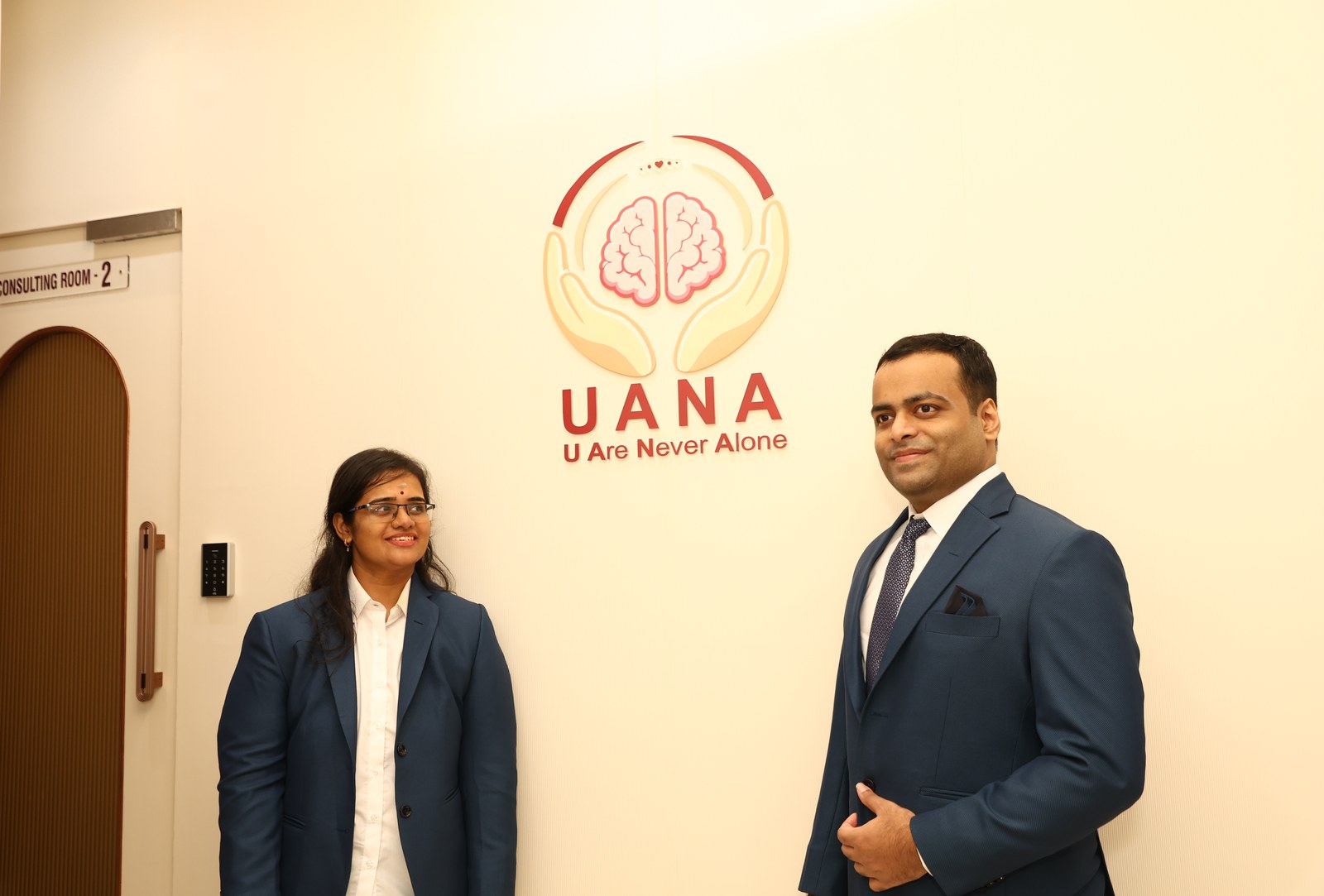 Sanjana Seetharaman Iyer and Dr. Seetharaman Iyer standing beside the UANA wall logo at the centre